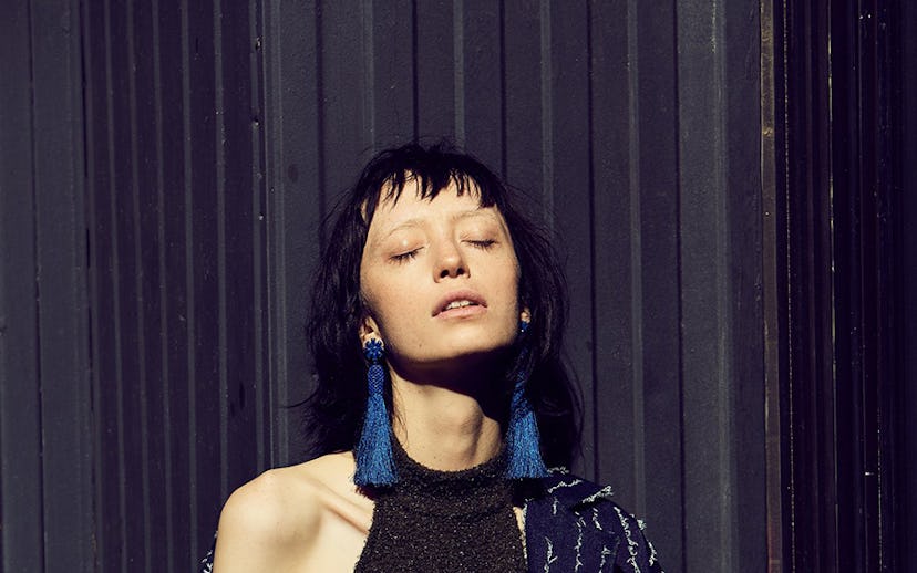 A model posing in a black sleeveless dress, with a navy blue, patterned, long jacket