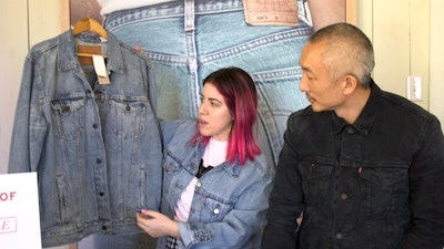 Woman with a brown/pink bob-length haircut showing a denim Levi's jacket to Jonathan Cheung who's we...