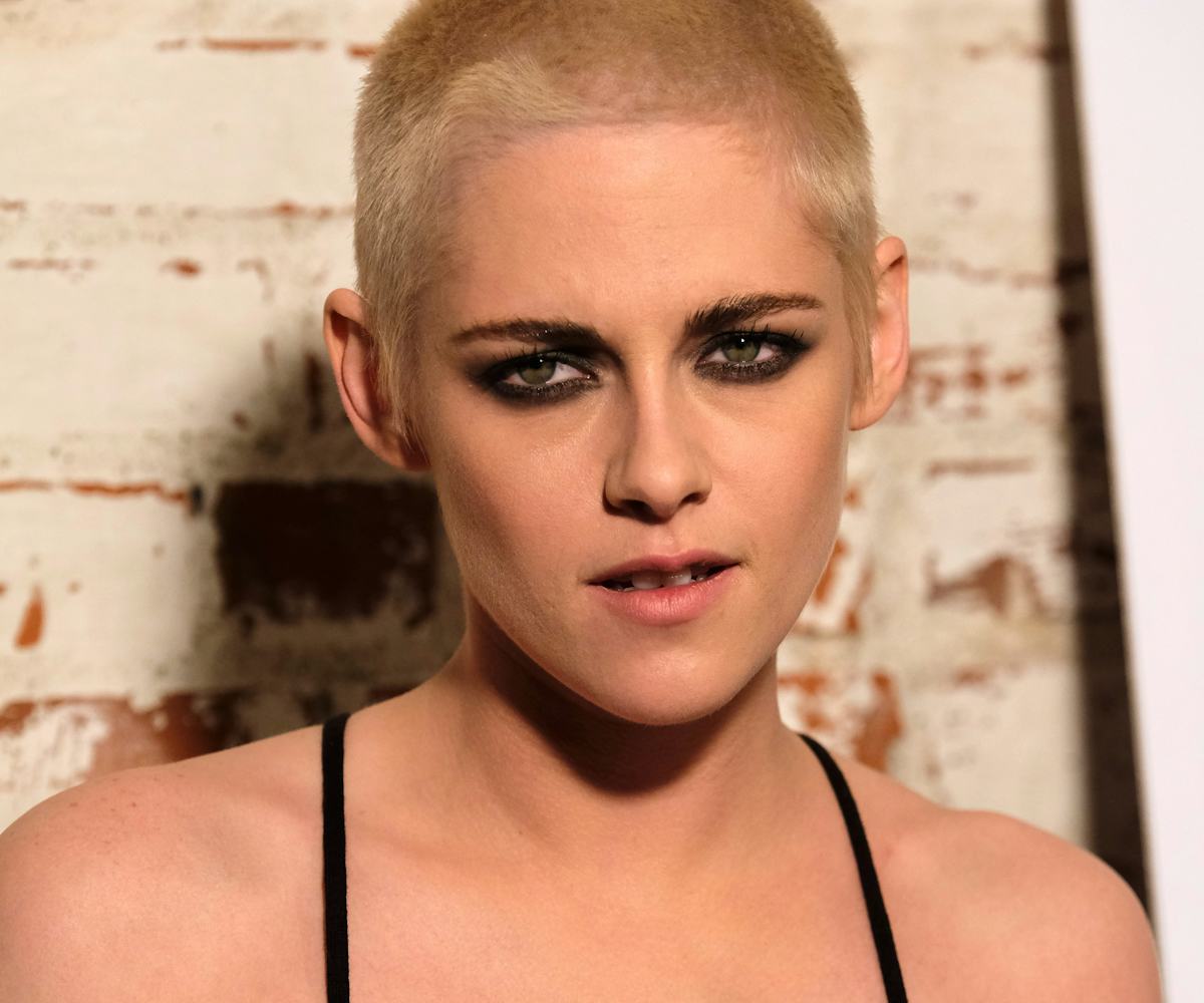 Kristen Stewart, with a short haircut, and smoky eye makeup, wearing a black spaghetti-strapped slip...