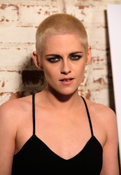 Kristen Stewart, with a short haircut, and smoky eye makeup, wearing a black spaghetti-strapped slip...