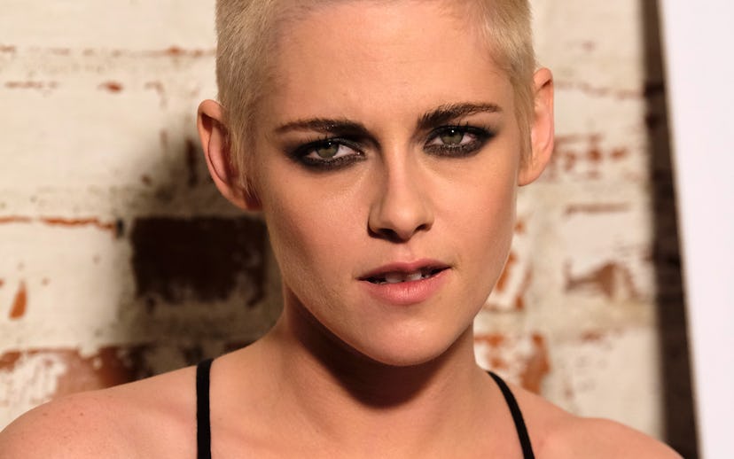 Kristen Stewart, with a short haircut, and smoky eye makeup, wearing a black spaghetti-strapped slip...