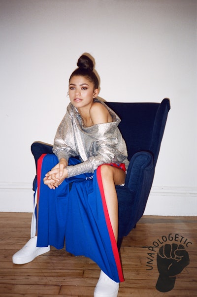 Zendaya sitting on an armchair wearing a long blue skirt in combination with a shiny shirt 