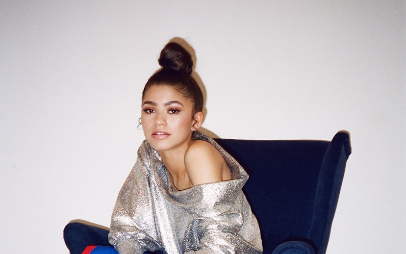 Zendaya sitting on an armchair while wearing a long blue skirt in combination with a shiny shirt
