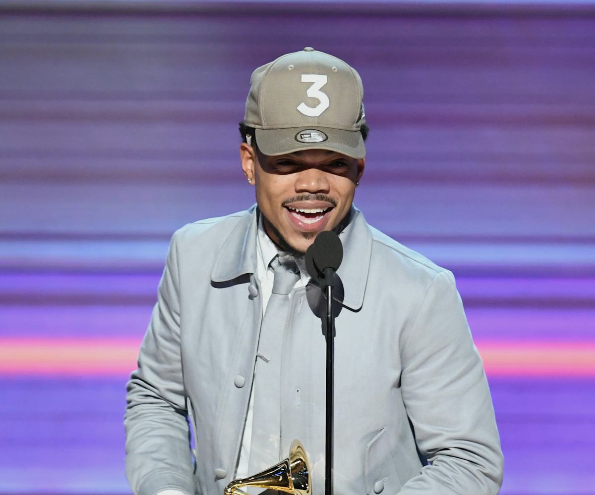 Chance the Rapper wearing a grey suit and a matching snapback at the Grammy’s while holding the awar...