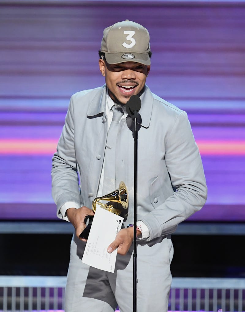 Chance the Rapper wearing a grey suit and a matching snapback at the Grammy’s while holding the awar...