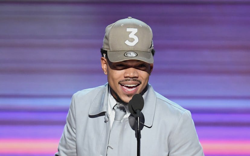 Chance the Rapper wearing a grey suit and a matching snapback at the Grammy’s while holding the awar...