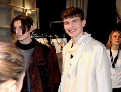 A male model in a white coat smiling while posing at the Berlin Fashion Week