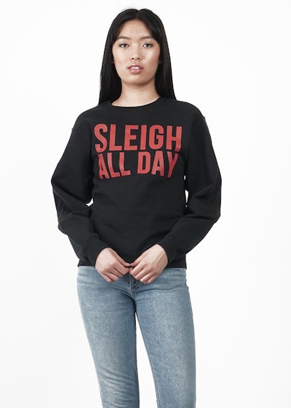 A female model posing in a black crewneck with a "Sleigh All Day" text sign