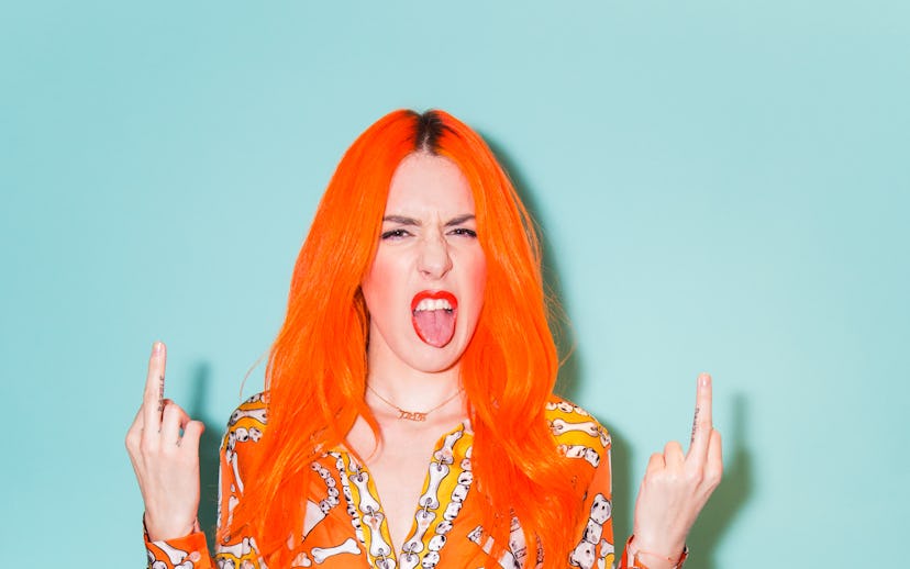 Kerin Rose Gold showing two middle fingers and sticking out her tongue in an orange shirt with a bon...