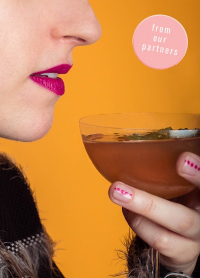 A woman holding a cup of a winter drink and wearing lipstick that complements it