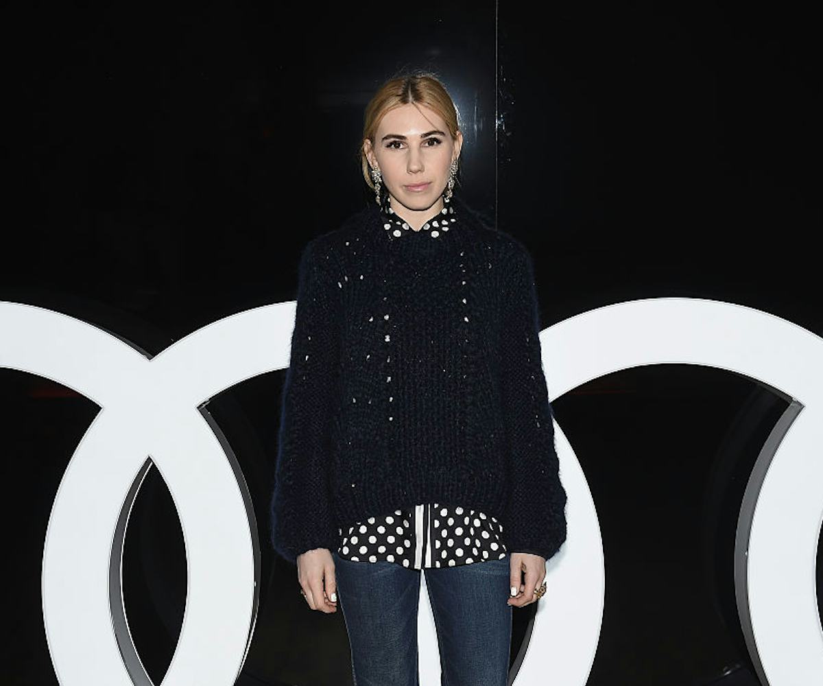 Zosia Mamet in a black sweater, a polka dot button-up and jeans 