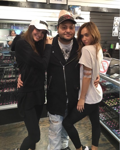 A man with his hands around the waists of two women all standing in the West 4 piercing studio surro...
