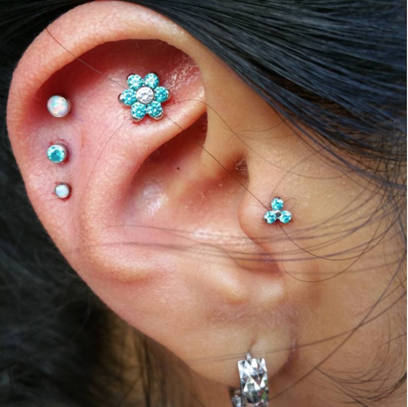 An ear pierced in six places with piercings of flowers and dots in white and baby blue