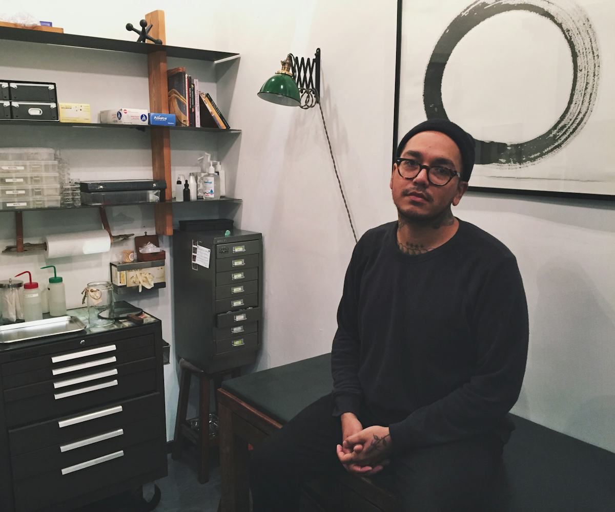 Adrian Castillo sitting in his piercing studio in a black shirt and a black beanie 