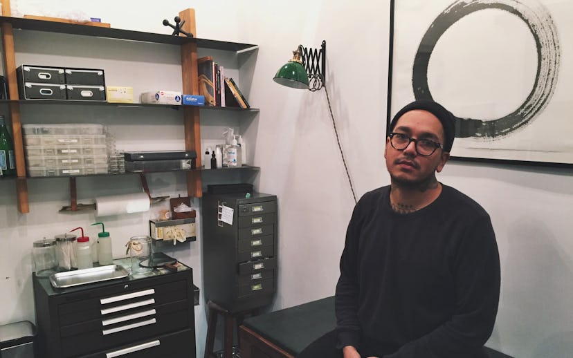 Adrian Castillo sitting in his piercing studio in a black shirt and a black beanie