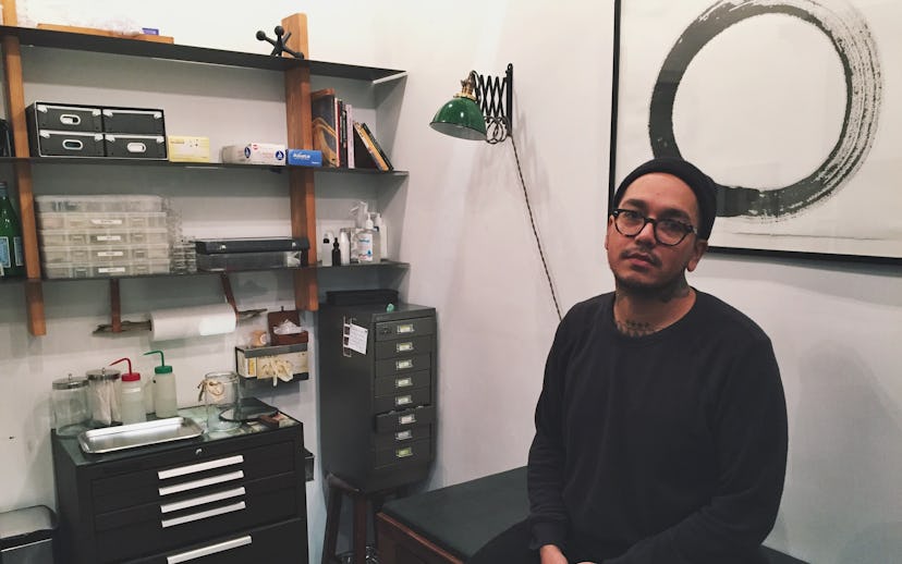 Adrian Castillo sitting in his piercing studio in a black shirt and a black beanie 