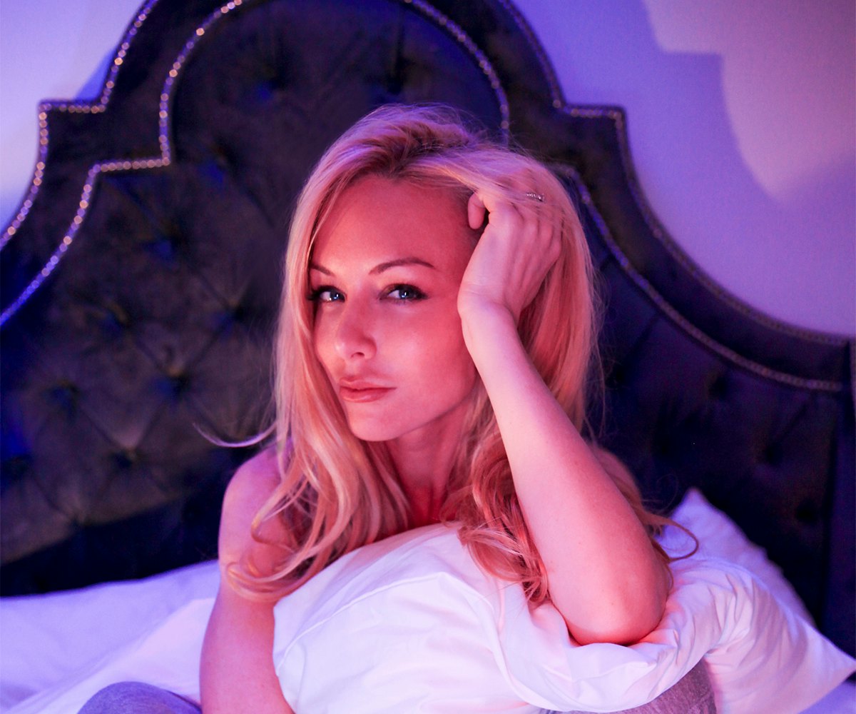 Kayden Kross sitting on the bed while holding the pillow