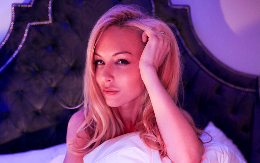 Kayden Kross sitting on the bed while holding the pillow