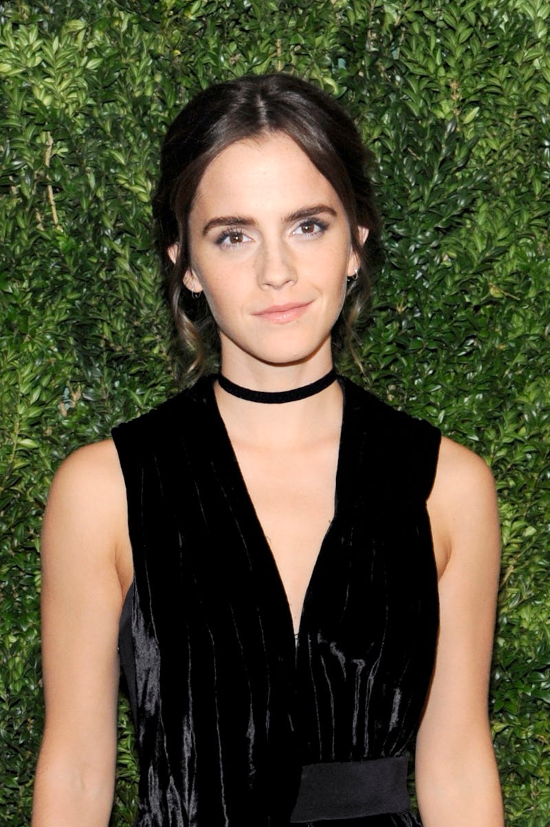 Emma Watson smiling while wearing a black dress and a black velvet choker in front of a green backgr...