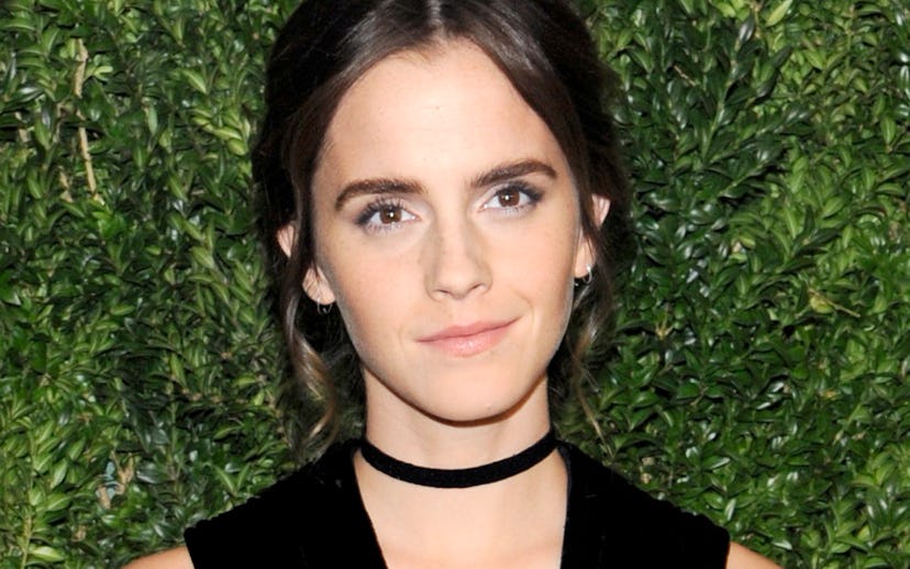 Emma Watson smiling while wearing a black dress and a black velvet choker in front of a green backgr...