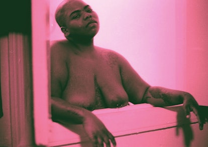 A naked bald woman standing leaned against a window