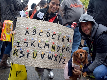 A dog dressed up as Eleven from Stranger Things next to a board with the alphabet and fairy lights o...