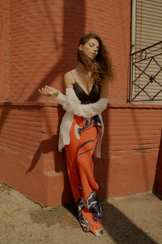 A woman posing while wearing orange pants and a black top