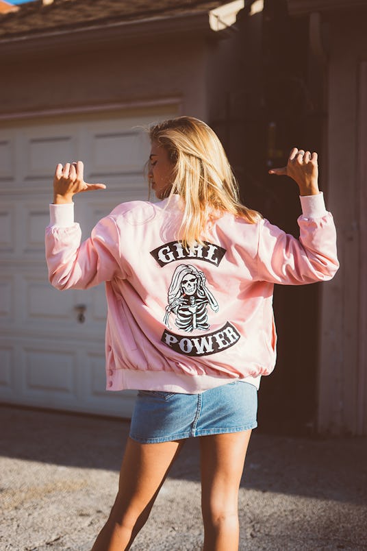 A blonde woman pointing at her back in a pink jacket from NYLONshop and Petals and Peacocks collabor...