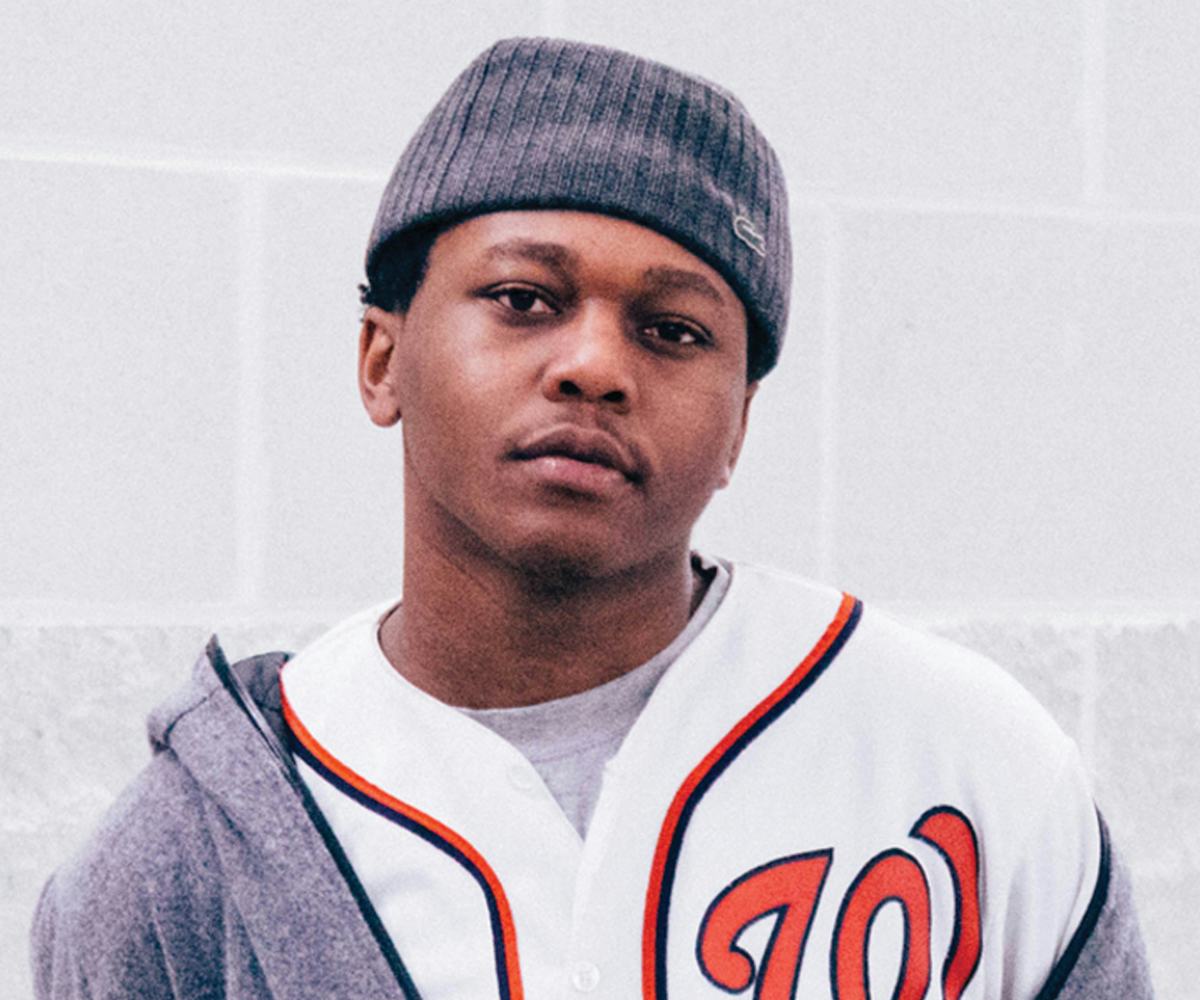 Innanet James in a grey hat, white baseball jersey and grey hoodie, looking at the camera.