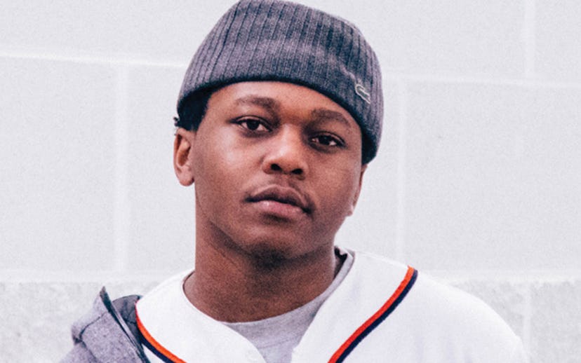 Innanet James in a grey hat, white baseball jersey and grey hoodie, looking at the camera.