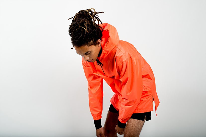 A male model posing while wearing a Tastemaker Collective orange Windbreaker jacket