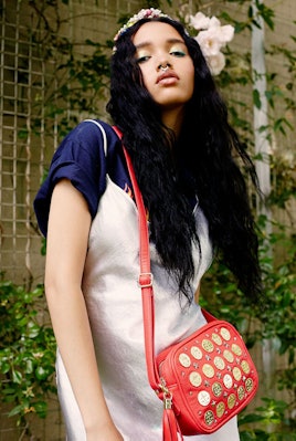A model in a silver slip on dress over a T-shirt showing off the red coin shoulder bag by Poppy Liss...