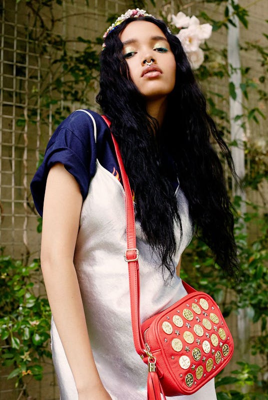 A model in a silver slip on dress over a T-shirt showing off the red coin shoulder bag by Poppy Liss...