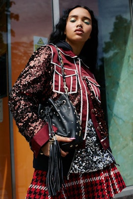 A model in a burgundy jacket with sequins with a red and white checkered skirt and a black coin buck...