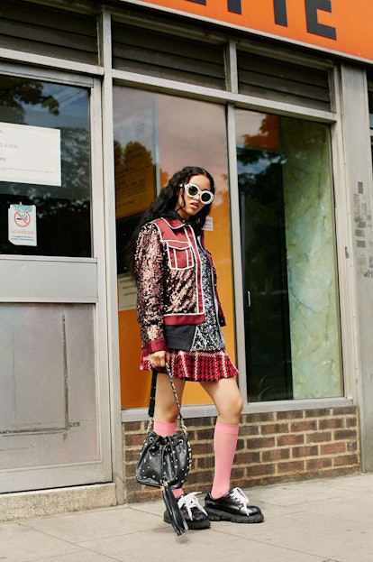 A model in a burgundy jacket and a red and white checkered skirt with her black coin bucket bag by P...