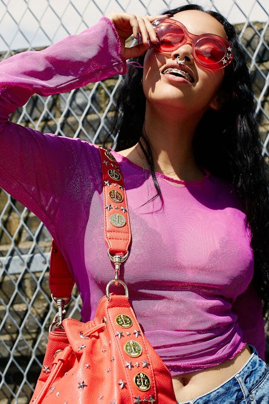 A model in a purple shirt matching red sunglasses with the red coin bucket bag by Poppy Lissiman
