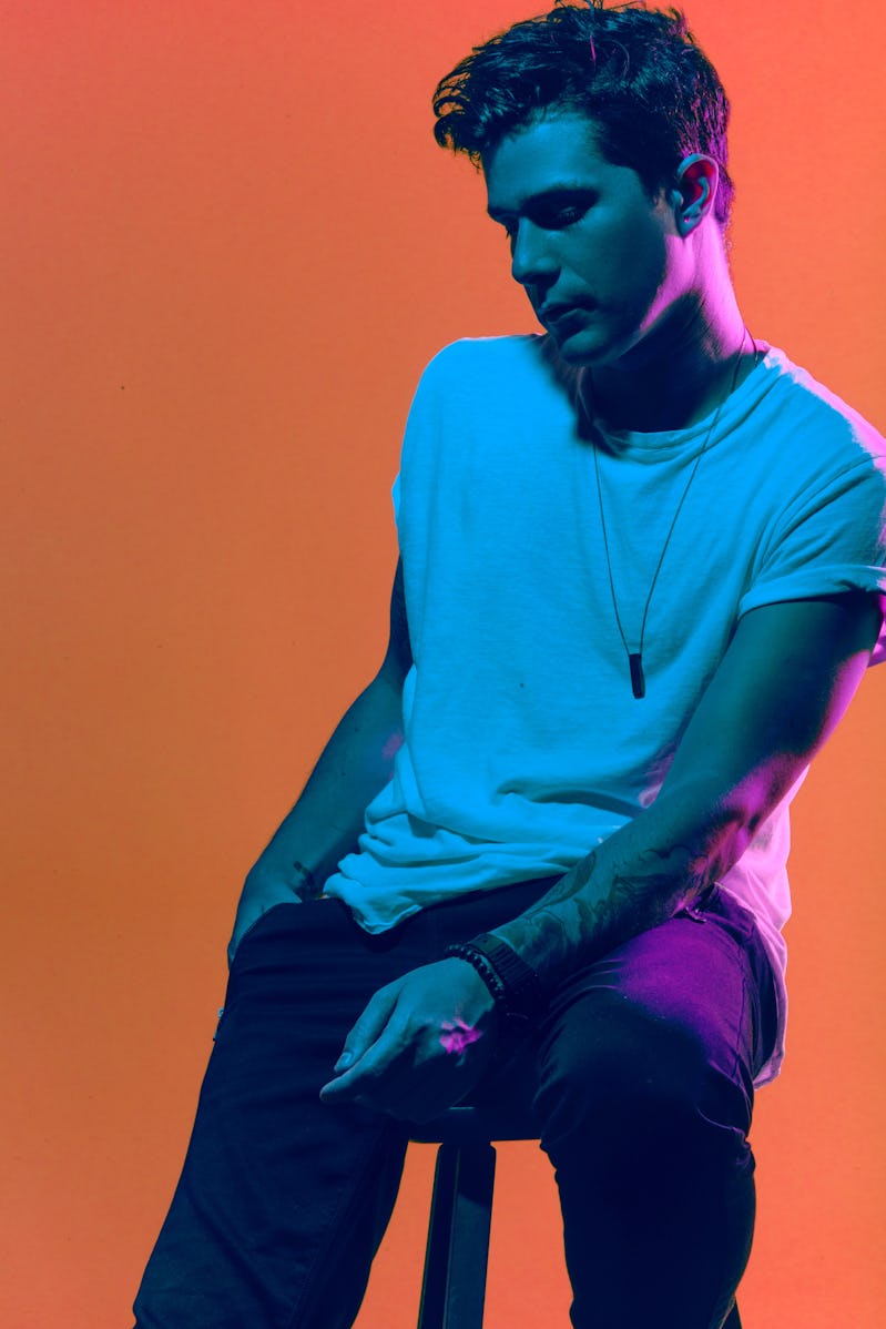 Le Youth sitting on a stool while wearing a white t-shirt and dark pants