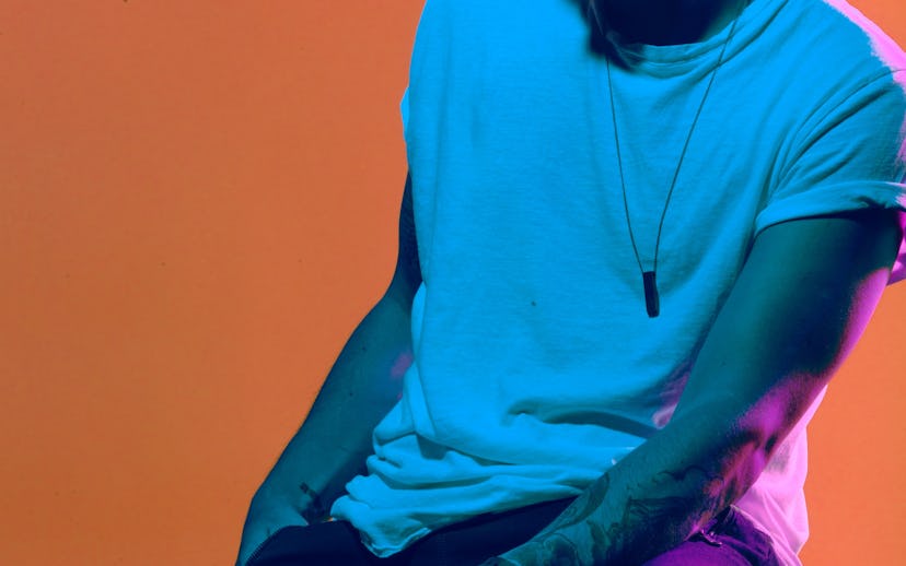 Le Youth sitting on a stool while wearing a white t-shirt and dark pants