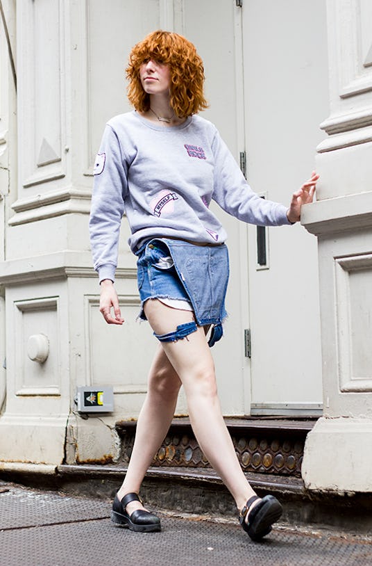 Claire Geist walking down the street in a grey cat hoodie and unbuttoned denim overall shorts 