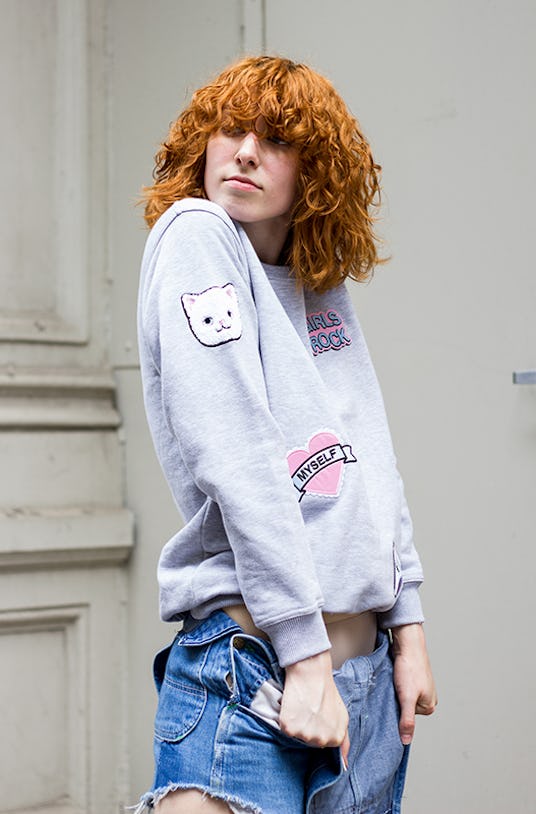 Claire Geist looking into the distance in a grey cat hoodie and unbuttoned denim overall shorts 