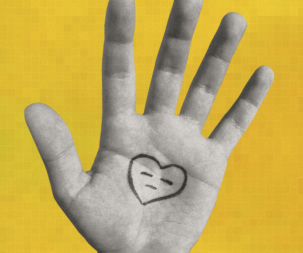 An open hand in front of a yellow background with a heart that is frowning drawn on it