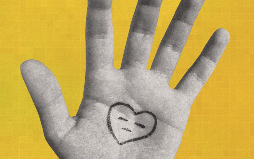 An open hand in front of a yellow background with a heart that is frowning drawn on it