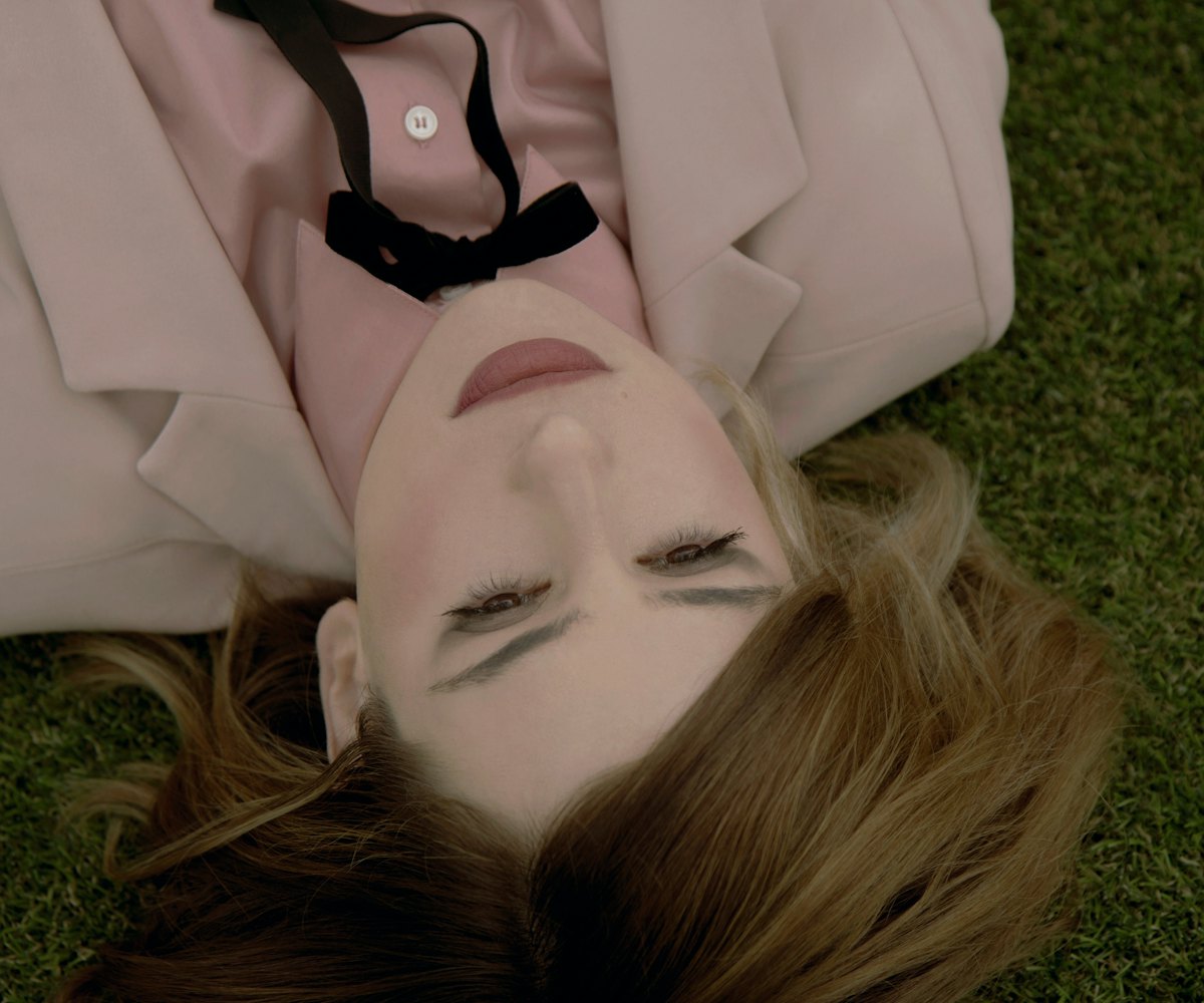 Kid Moxie lying on the grass in a pink button up shirt 