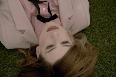 Kid Moxie lying on the grass in a pink button up shirt 