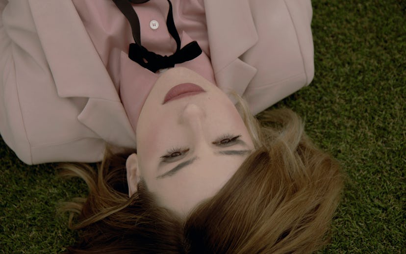 Kid Moxie lying on the grass in a pink button up shirt