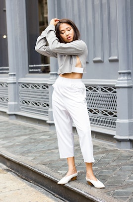 A girl posing while wearing a grey shirt, white pants, and white ballet flats
