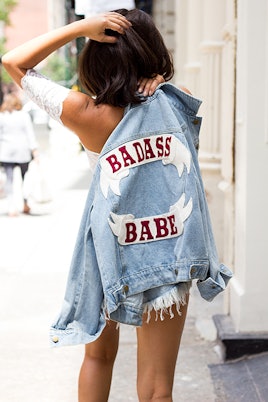 A girl walking down the street while wearing a white top and a denim jacket with a "Badass babe" tex...