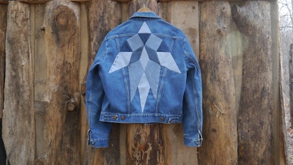 Blue denim jacket designed by Christi Johnson hanging on a wooden wall