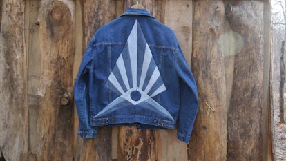 Blue denim jacket with a triangle designed by Christi Johnson hanging on a wooden wall