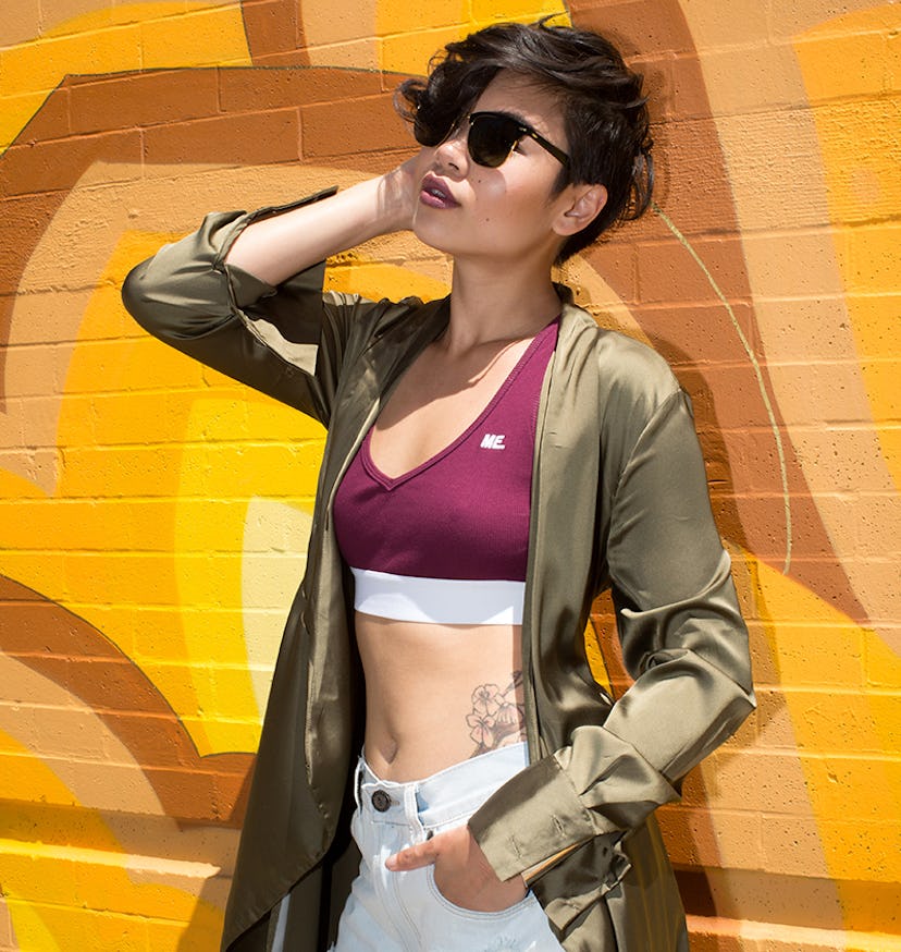 Lynn Kim posing in light ripped jeans, a burgundy top, and an olive jacket while leaning against an ...
